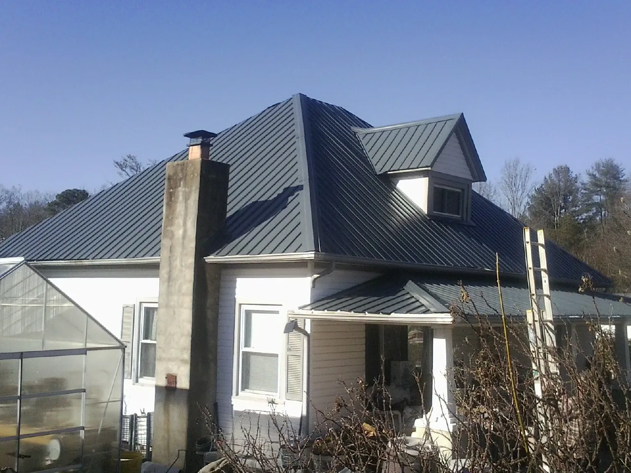 Dark blue standing seam metal roof on a white farmhouse with dormer — Slate & Tile Roof Repair by Roofing Brothers in North Sutton