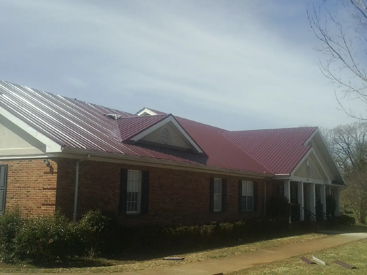 Red metal roof with gabled entries on a long brick building, from a Hail Damage Roof Repair job in North Sutton