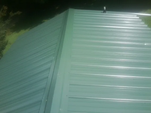 New green metal panels meeting at the ridge of a roof — Flat Roof Repair work by our crew in North Sutton