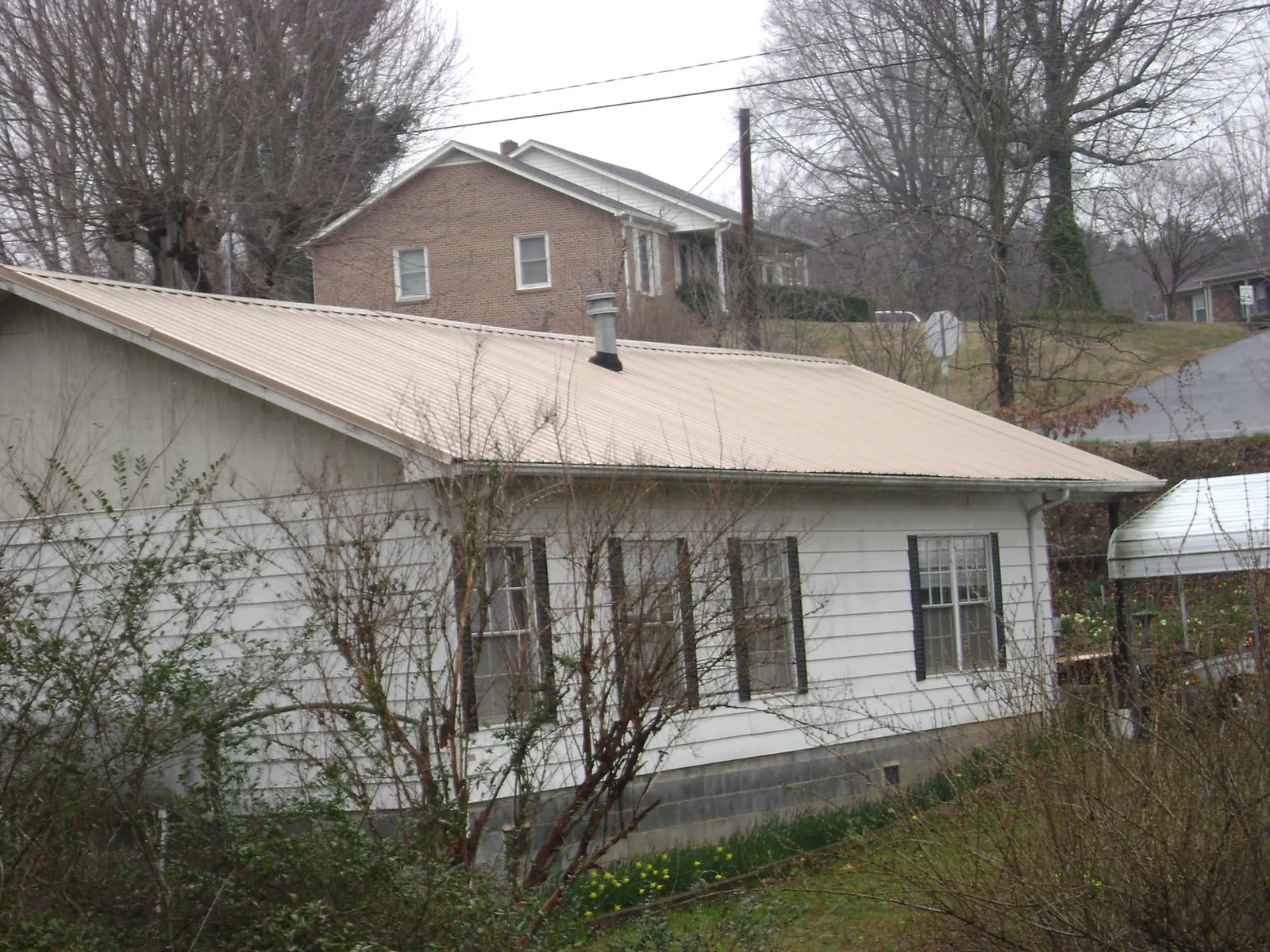 Tan metal roof on a white sided house set into a hillside — Commercial Roofing by Roofing Brothers in North Sutton